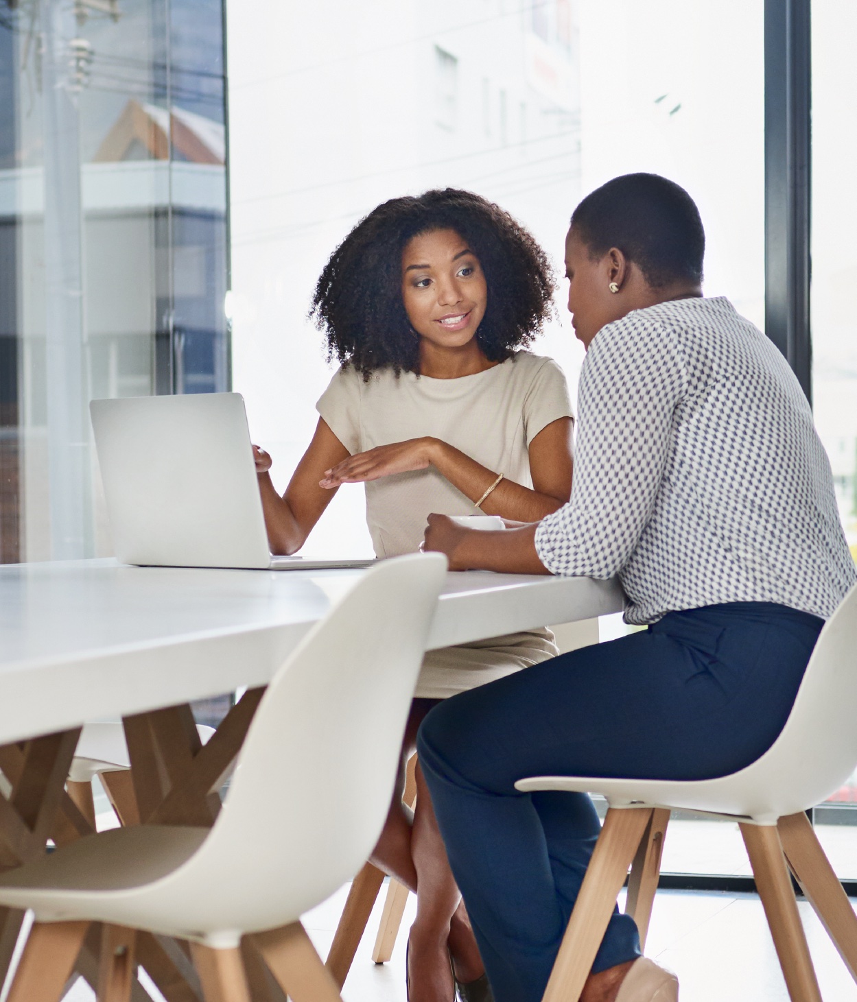 Two Black businesswomen discuss a project in an office with a laptop.