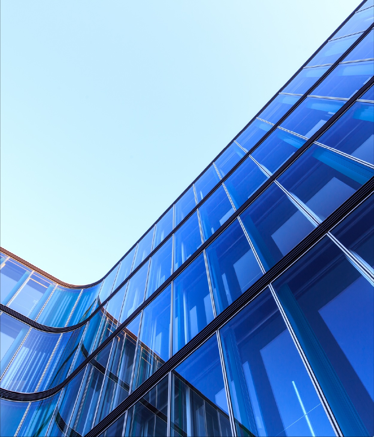 Low-angle photo of the curved glass façade of an office building.