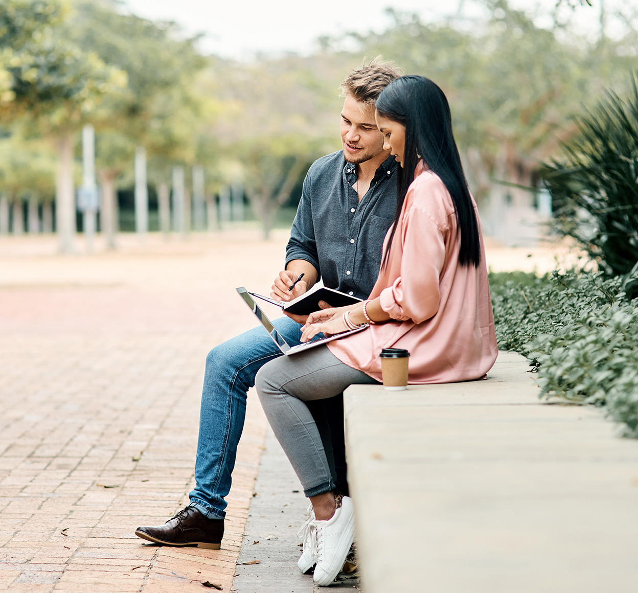 Shot of two young  students using a laptop while sitting outside on campus